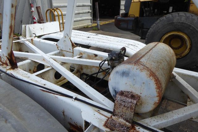 Truck trailer frame with rusted cylindrical tank and hydraulic components. Visible white metal framework and rust spots.