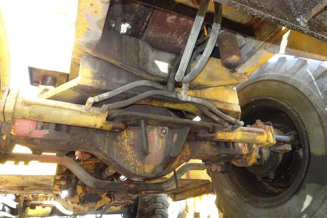 Grove RT58 undercarriage showing steering linkage, hydraulic lines, and differential housing with visible wear and rust-like patina.