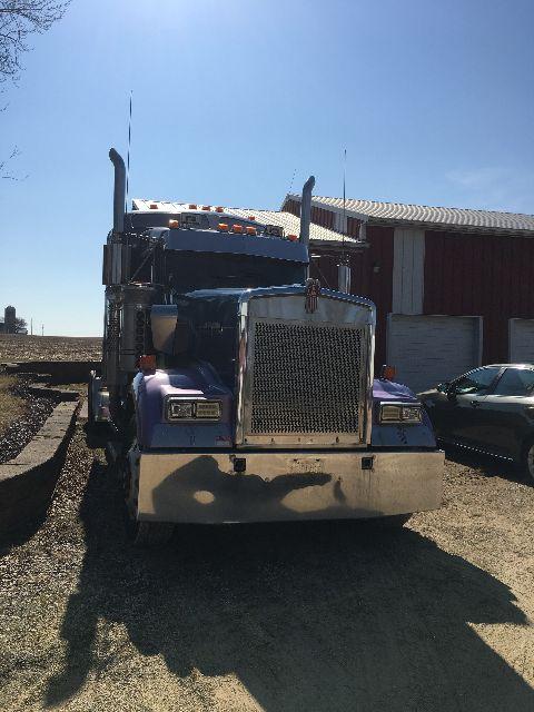 Kenworth W900L conventional sleeper truck front view in blue with chrome grille and large bumper.
