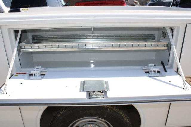 Truck service bed with open storage compartment showing a long aluminum/rack-like bracket and supporting rails.