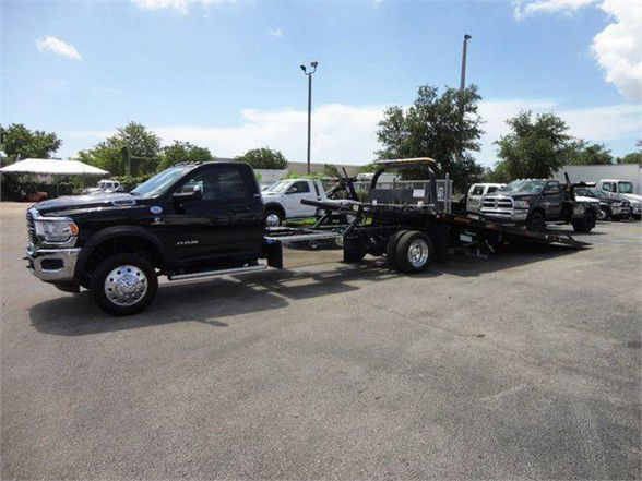 Black 2024 Ram 5500 SLT tow truck with flatbed trailer in a dealership lot.