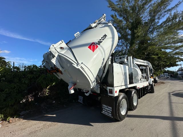 Vacuum truck with a large tilted cylindrical tank labeled VAC CON and dual rear axles on a street.