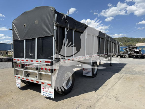 2022 Reitnouer Big Bubba trailer in a lot with black tarp sides and dual rear wheels. Side view shows long flatbed with covered cargo area and rear bumper.