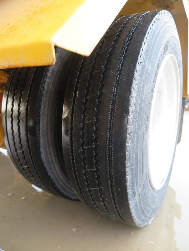Wheel close-up on a yellow truck with dual rear wheels and a white rim. visible tread marks on the tires.