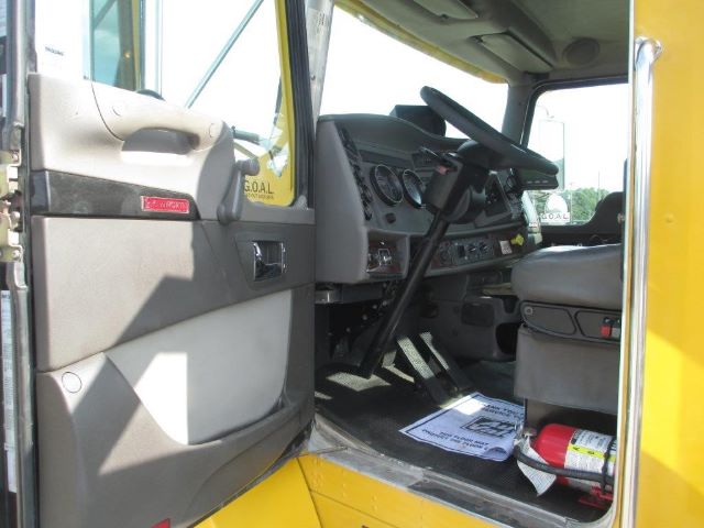 Kenworth T300 truck interior showing driver seat and dashboard with steering wheel and gauges; yellow exterior visible at doorway.