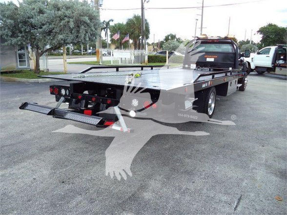 Flatbed tow truck with ramp and hydraulic tilt system. Visible text includes partial phone number and dealership watermark overlay.