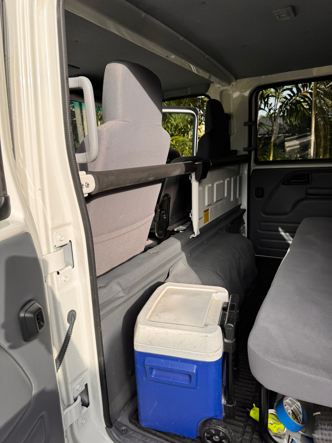 Isuzu NQR interior side passenger area showing rear bench seat, grab bar, cooler, and utility area with plastic paneling.