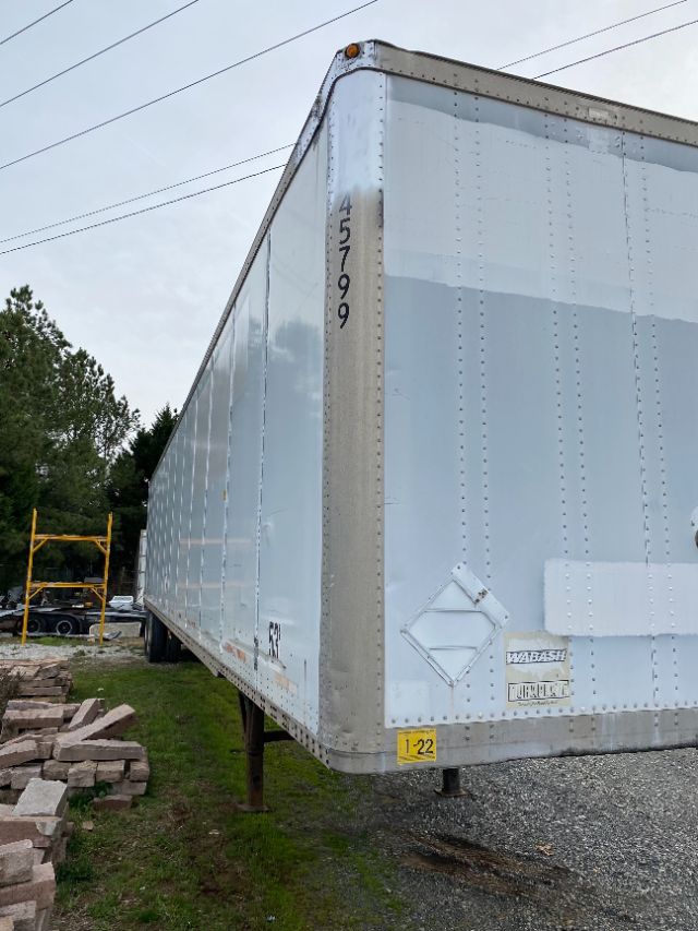 White Wabash trailer with Duraplate front showing vertical riveted seams and corner post; numbers 45799 along front edge; yellow safety placard and Wabash/HydroPlate logos visible.
