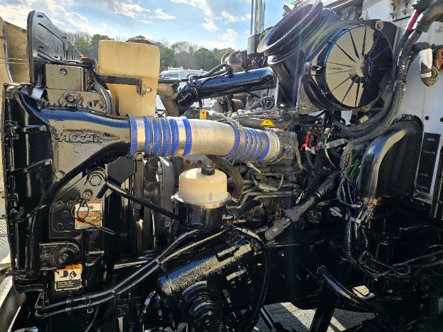 Peterbilt truck engine bay with large blue flexible hose, white plastic reservoirs, and various black hoses and components visible.