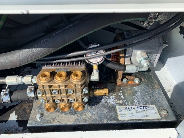 Hydraulic valve manifold with multiple brass ports and hoses in a compact machinery setup. Gauge and metal base plate with label plate.