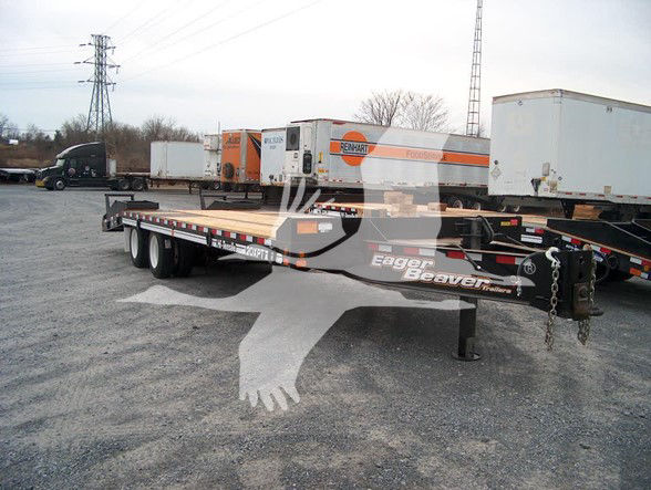 Flatbed trailer with Eager Beaver logo and 20Xpt model, long wooden deck, trailer hitch, and dual rear axles visible in a storage lot.