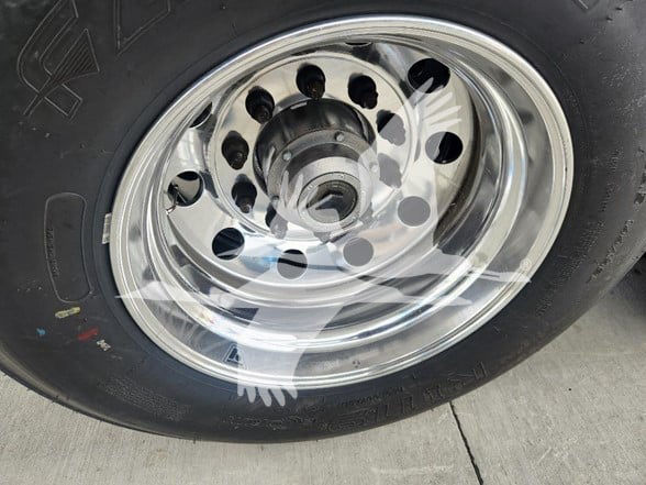 Wheel and tire of a new dump trailer showing chrome hub with circular lug holes and black tire.