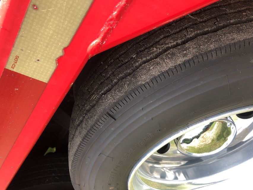 Wheel and tire close-up on red Peterbilt truck fender with chrome hubcap and textured tire tread.