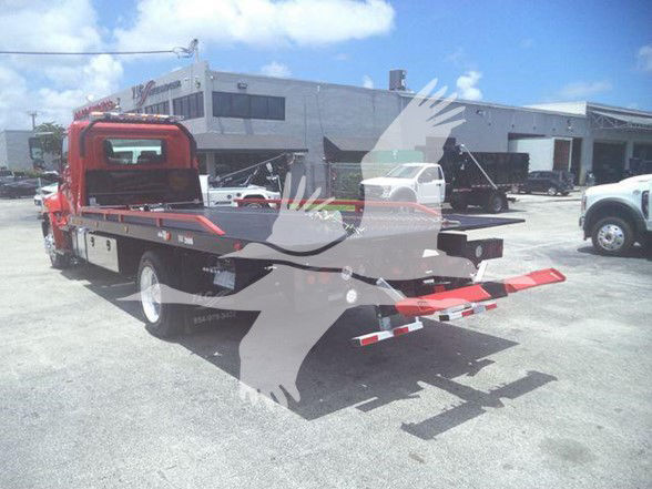 Truck bed with red and black colors, tow truck style flatbed on a 2020 Hino 268A seen in a dealership lot.