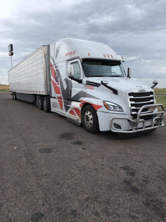 Truck cab of a 2018 Freightliner Cascadia with a large aluminum trailer in a parking lot.