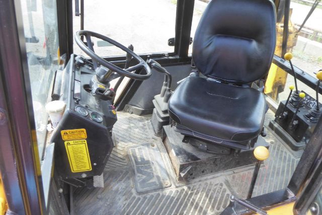 Cab interior of Massey Ferguson backhoe showing steering wheel, operator seat, and control levers in a compact cabin.