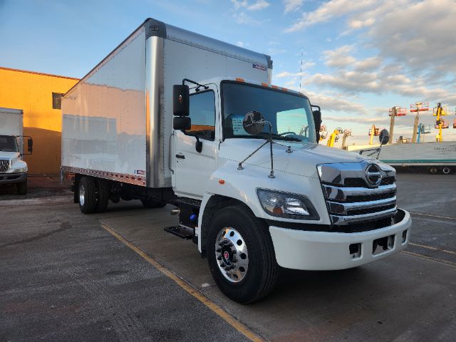 Box truck with white cab and large white box body, Hino emblem on grille, front view angled to right, black mirrors, dual rear wheels.