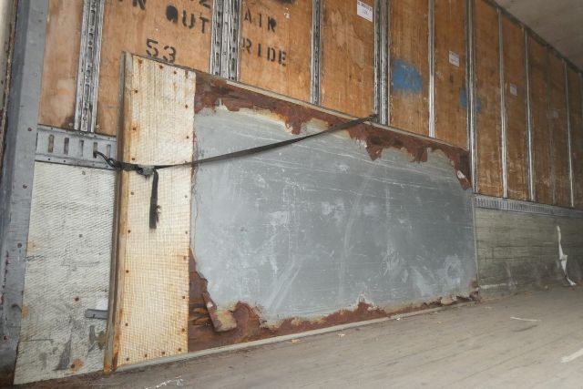 Great Dane trailer interior side wall with worn metal paneling and wooden framing inside a trailer.