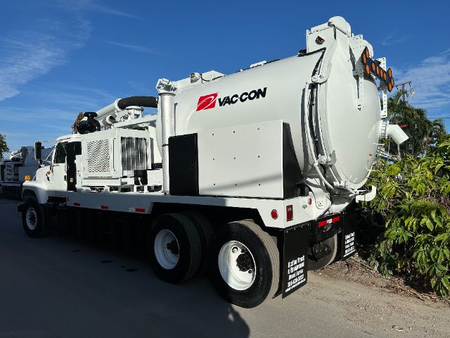 VacCon vacuum truck with large rear tank and hose reel, white color, VacCon branding on side, side mirrors, and dual rear wheels visible.