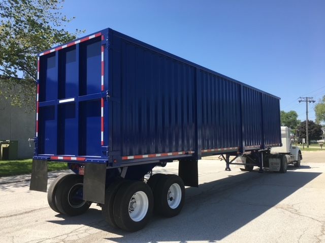 Large blue 40 ft square dump trailer attached to a truck, showing dual rear axles and tall metal walls with red-white reflective tape along edges.