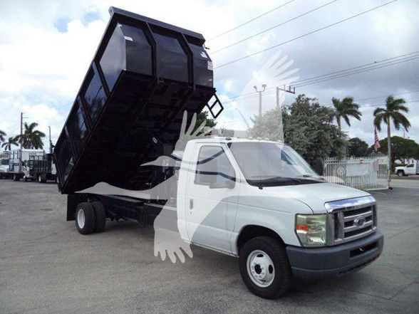 Ford E-450 dump truck with a raised black dump bed in a dealership lot.