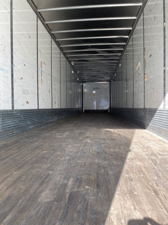 Interior of an empty cargo trailer with Duraplate walls and wooden floor, long narrow space, rear door visible at far end.