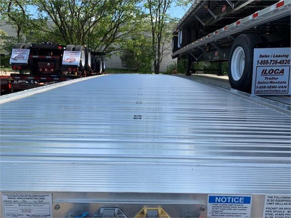 Flatbed trailer deck on a 2024 Fontaine ALL ALUMINUM 48FT trailer showing aluminum deck with side rails and warning notices.
