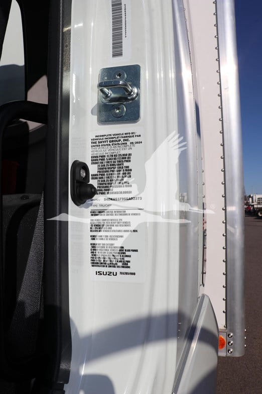 Isuzu truck door jamb showing compliance label and latch with barcode on white painted body.