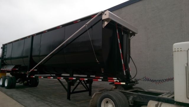 Dump trailer with black round-bottom 40 ft Great Dane design; visible wheels and frame, rear tailgate area, and support structure.