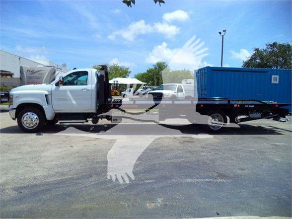 Truck with a white cab and a blue container trailer. Side view showing front and rear tires, clear sky, and dealership lot. Overlay watermark obscures center.