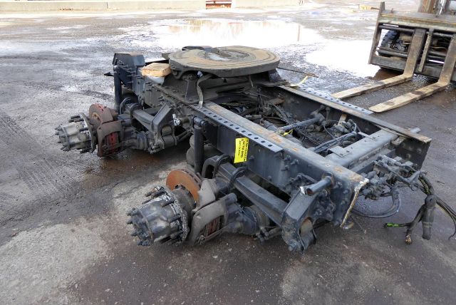 Truck rear axle assembly with Meritor MT4014X components, drum brakes, brake rotors, and suspension framework visible; fuel lines and wiring present; yellow tag on frame rail.