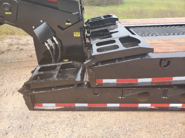 Lowboy trailer deck side with Kingpin area and steps; appears to be a 2020 Atoka RGN-553-S. Visible labels include small yellow warning decals on the hydraulic area and reflective red/white striping on the edge.