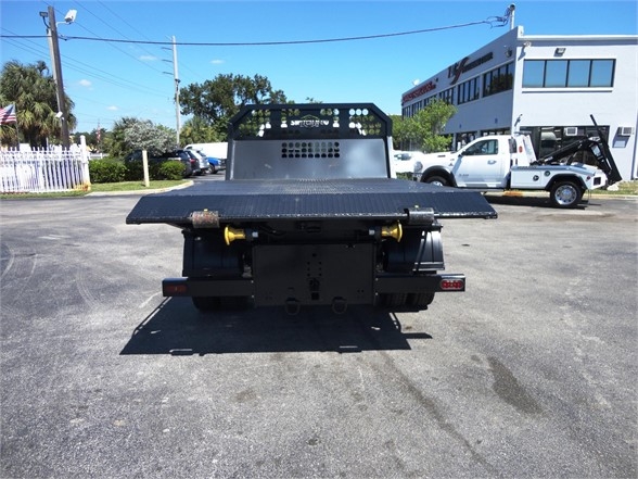 Ram 5500 HD hooklift truck rear view with flatbed and bumper, yellow hydraulic pins, and perforated cab guard.