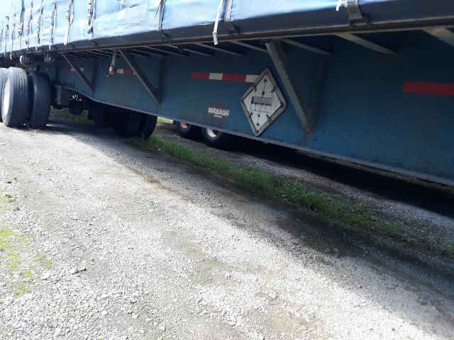 Trailer underside with blue side rails and a diamond-shaped placard, tire axles visible, gravel ground beneath.