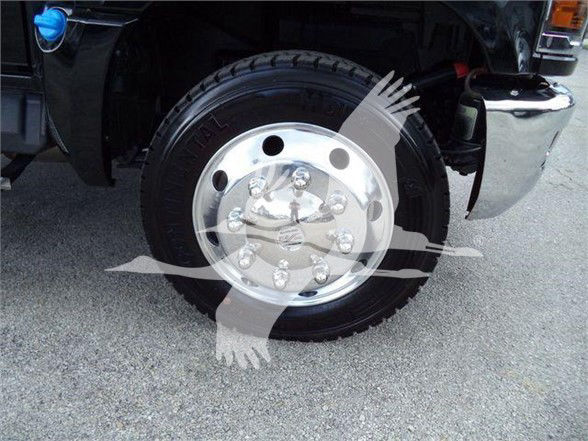 Truck wheel and chrome hubcap with lug nuts on Silverado 6500HD front tire. Partial fender and bumper visible.