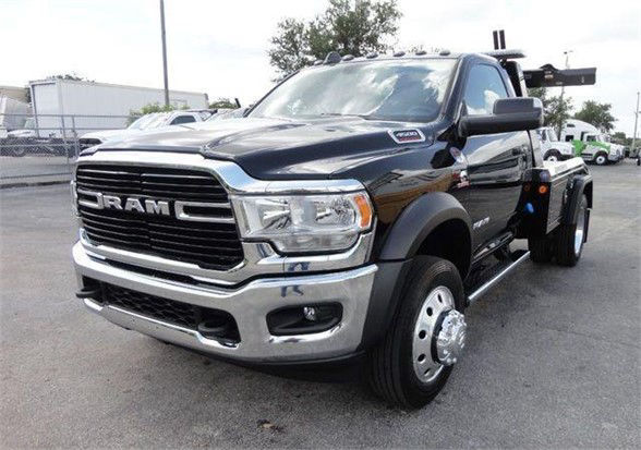 Ram truck front-left view showing bold grille with RAM lettering and chrome bumper; dual rear wheels on tow truck chassis; black exterior with chrome accents.