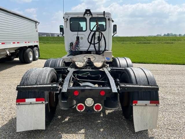 Truck chassis rear view showing fifth-wheel coupling and dual rear axles under Freightliner Cascadia cab; wiring harnesses and mud flaps visible.