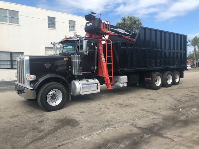 Peterbilt 388 dump truck with a red crane/boom attachment and black dumping bed, side view showing rear wheels and cab details.