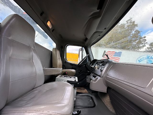 Cab interior of a Freightliner M2 truck showing driver and passenger seats, dashboard, steering wheel, and windows.