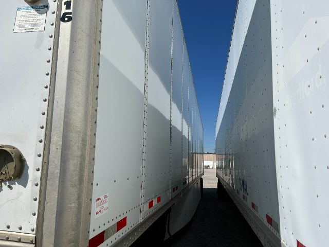 Trailer side-by-side view showing white cargo trailers with riveted panels and reflective red/white safety markers; narrow gap between two trailers with clear blue sky