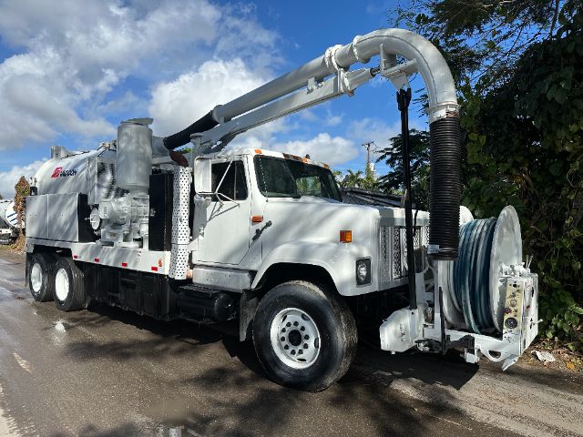 Vacuum truck with large hose reel and articulated boom mounted on a white International chassis, side view showing pump area and hose reel.