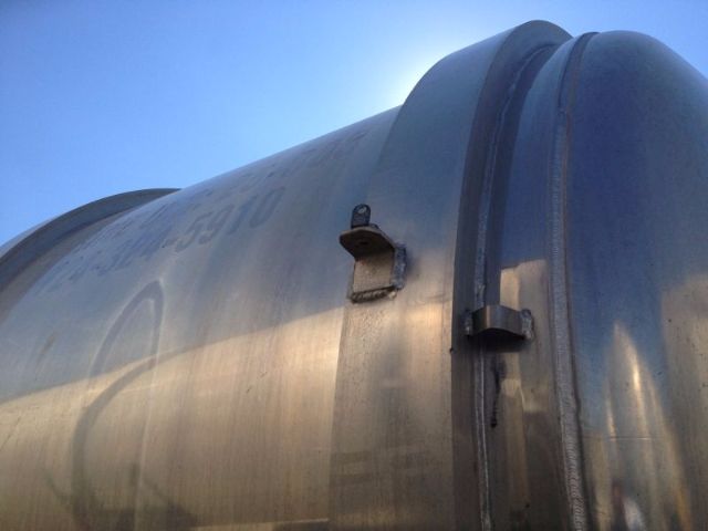 Industrial vacuum tank trailer with metal cylindrical body and seam near the door, showing a mounting bracket and latch.