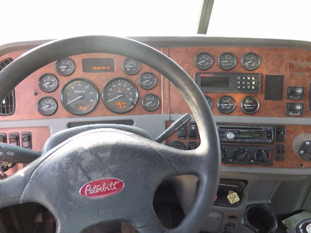 Peterbilt truck cab interior dashboard with multiple gauges, steering wheel, and woodgrain panel.