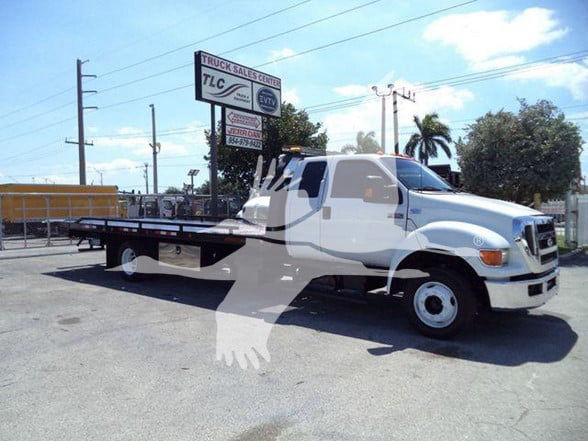 Ford F-650 XLT tow truck in a dealership lot with a flatbed, side view showing the cab and long bed.