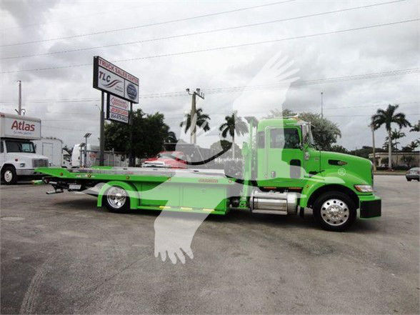 Green 2022 Peterbilt 337 tow truck with flatbed, side profile, showroom lot in background.