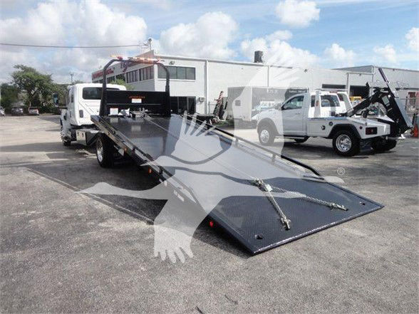 Truck bed tow truck with flatbed platform and ramp, International MV tow truck in a dealership lot.