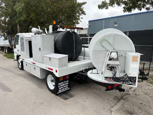 GMC W5500 vacuum service truck with large circular vacuum reel and equipment on flatbed; white metal body, tanks, and hoses visible.