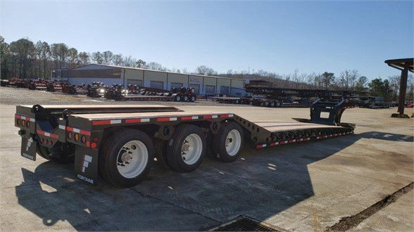 Fontaine lowboy trailer with long flatbed and roller paver trailer equipment in background, three axles, dual rear axles visible.