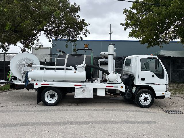Truck-mounted industrial vacuum unit on a white GMC W5500 chassis with large vacuum tank, hoses, reels, and exhaust stack visible.