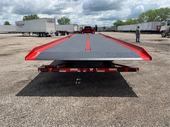 2024 drop deck container delivery trailer, single axle, rear view showing flatbed with red accents and loading ramps, in a lot with other trailers.
